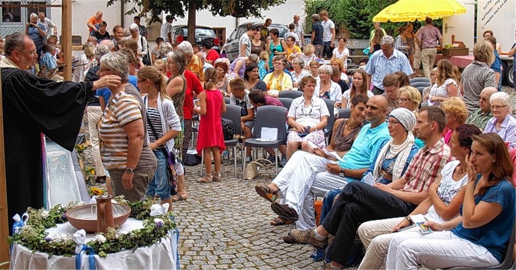 Taufgottesdienst der anderen Art: Pfarrer Veit und seine Kirchengemeinde feiern gemeinsam mit den acht jungen und alten Täuflingen.