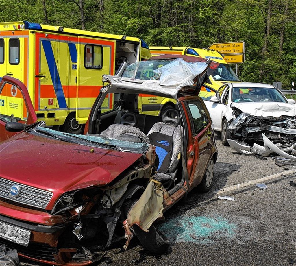 Totalschaden: Im Vordergrund der Wagen des 64-Jährigen, der in seinem Auto eingeklemmt wird und von der Feuerwehr, die das Dach öffnet, befreit werden muss.