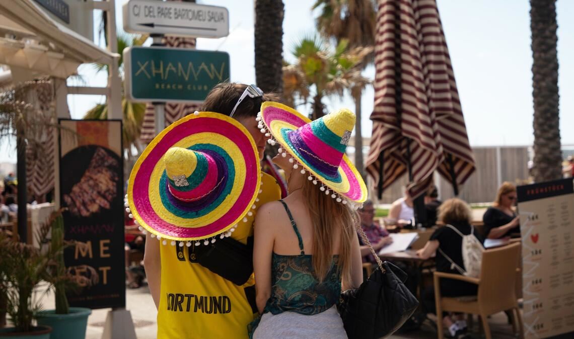 Touristen mit bunten Hüten stehen beim Start der Ballermann-Saison auf Mallorca an einer Bar.