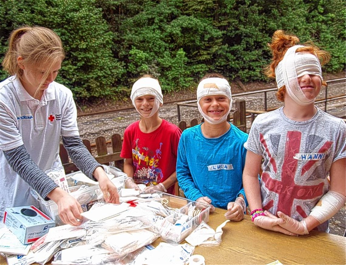 Trotz ihrer „Kopfverletzung“ sind diese Teilnehmer am Kinderferienprogramm sichtlich fröhlich. Sie erfahren aber von der DRK-Mitarbeiterin auch, wie schlimm Blessuren nach einem echten Sturz vom Fahrrad ausfallen könnten, wenn der schützende Helm fehlt.