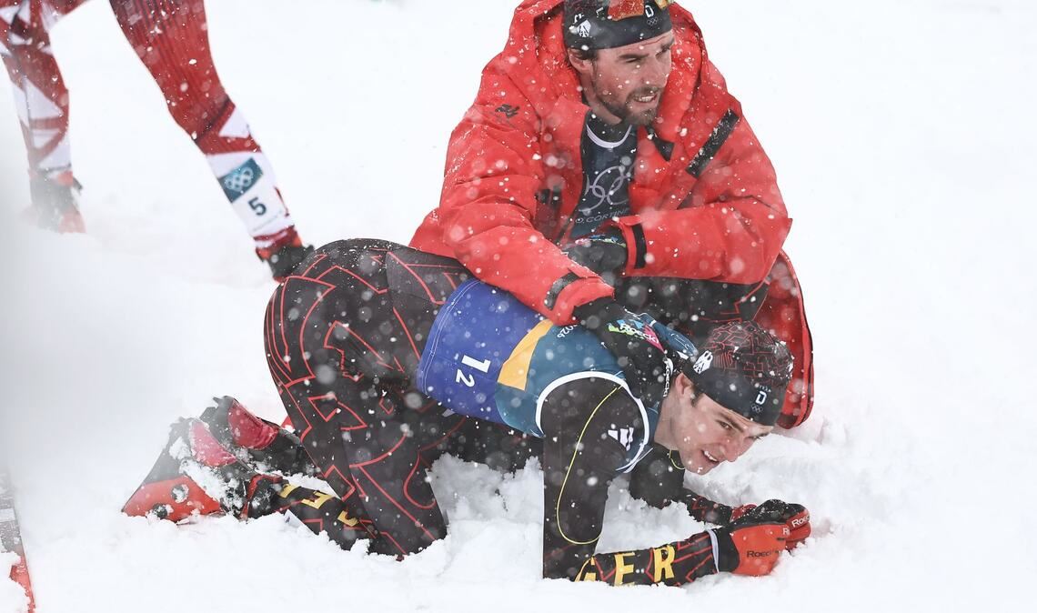 Vinzenz Geiger liegt im Schnee und wird von Teamkollege Johannes Rydzek getröstet.