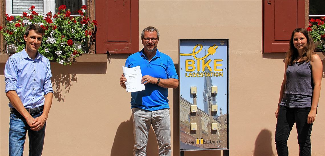 Vor der E-Bike-Ladestation am Rathaus: Übergabe der Energie- und CO2-Bilanz an Bürgermeister Andreas Felchle (Mitte) durch Björn Ehrismann, Leiter der Kommunalberatung des Energie- und Bauberatungszentrums Pforzheim/Enzkreis (ebz), und Klimaschutzmanagerin Lisa Andes.privat