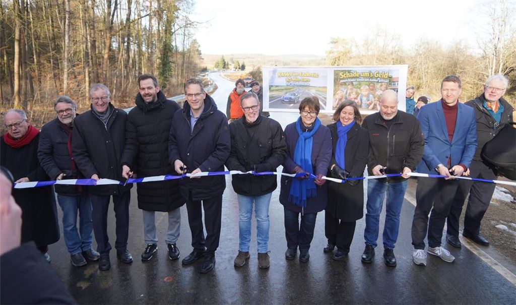 Während die Offiziellen um die beiden Landräte Roland Bernhard (3.v.li.) und Bastian Rosenau (4.v.li.) das Band durchschneiden, positionieren sich im Hintergrund die Kritiker des Projekts.