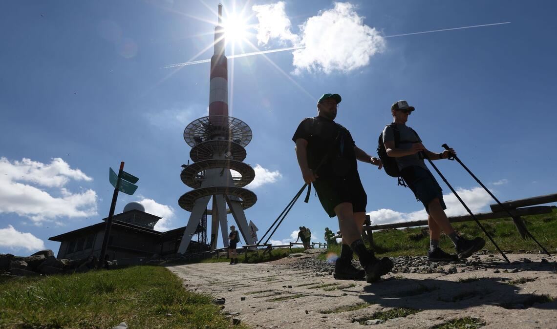 Wanderer gehen bei strahlendem Sonnenschein über einen Weg auf dem Brocken, im Hintergrund steht der Fernmeldeturm.