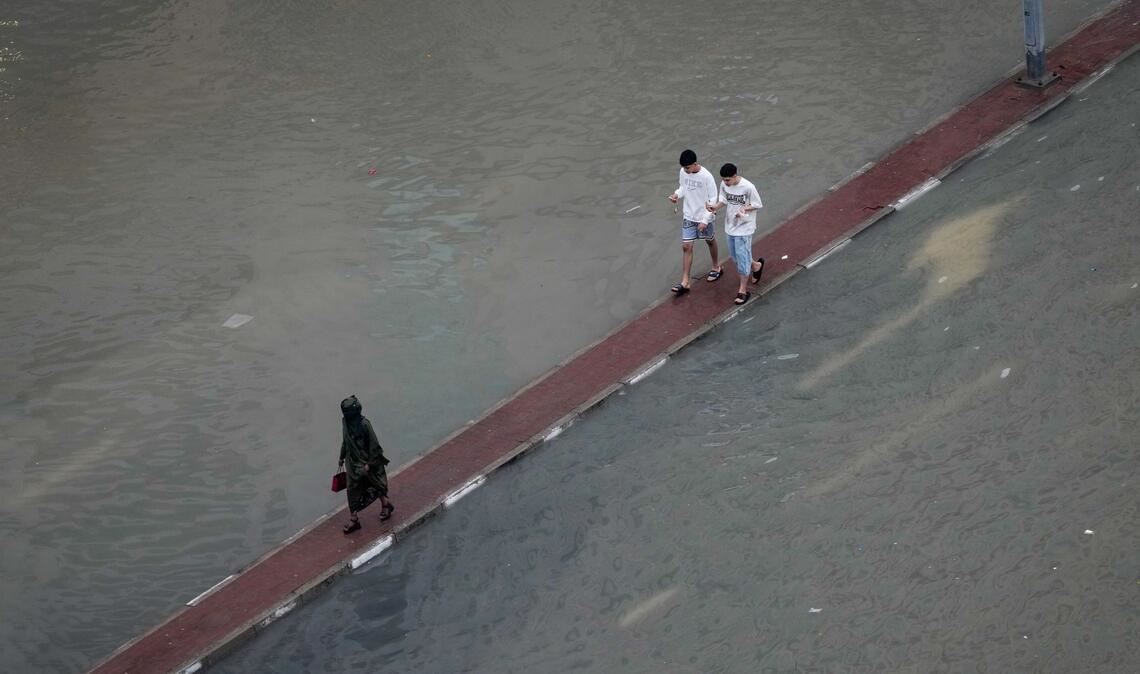 Wasser auf der Fahrbahn: Passanten in Dubai suchen auf dem Fahrbahnteiler einen trockenen Weg nach Unwettern