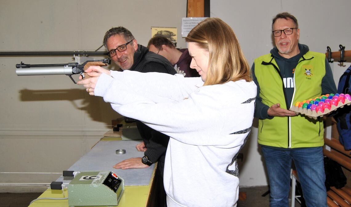 Wer ins Schwarze trifft, bekommt ein Ei: Hier steht eine Schützin mit der Luftpistole am Schießstand. Zur Freude von Oberschützenmeister Edgar Müller (re.) und Schießleiter Frank Siegrist kommt das Ostereierschießen bestens an. Foto: Haller