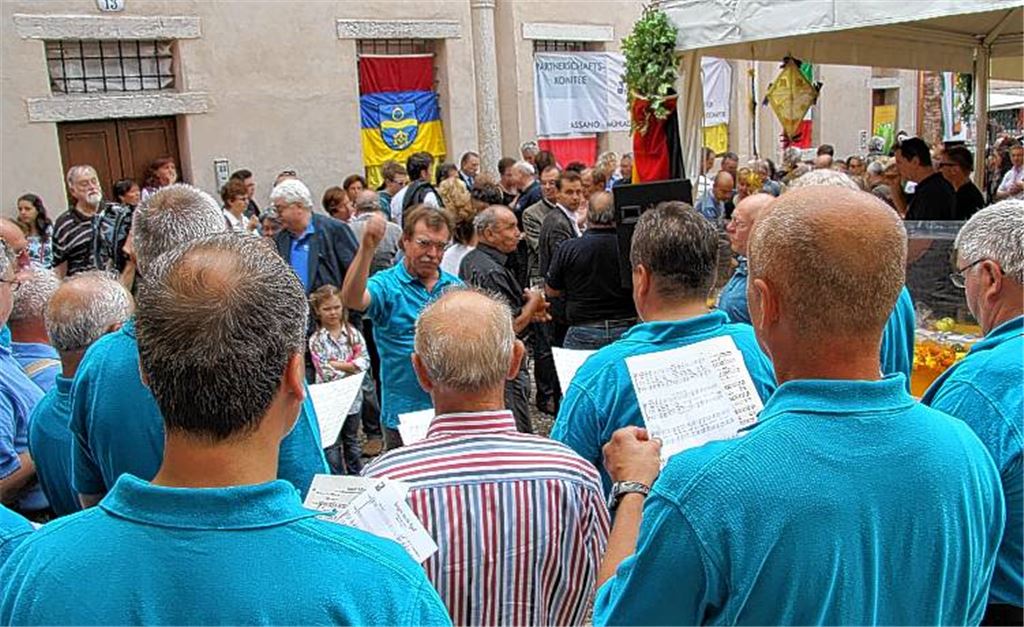 Wiedersehen in Bassano del Grappa: Der ehemalige Oberbürgermeister Klaus Schönfeld dirigiert den Chor des MGV Bubenorbis, während der aktuelle Oberbürgermeister Frank Schneider am Mühlacker Stand auf der Fiera Franca den Fassanstich begleitet.