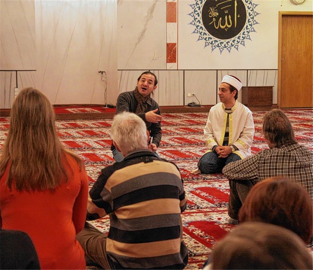 Yilmaz Cebeci, Sprecher der Moscheegemeinde in Maulbronn (li.) steht einer Gruppe von Konfirmanden im islamischen Gotteshaus im Gewerbegebiet „Talweg“ Rede und Antwort. Auch der Imam, der Vorbeter, nimmt sich Zeit für die kleine Besuchergruppe. Bevor die Gäste den Gebetsraum betreten, ziehen sie ihre Schuhe aus. Für die Muslime hängen Gebetsketten auf einer Stange bereit.