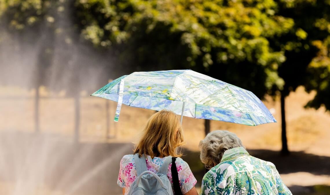 Zwei Frauen schützen mit einem Regenschirm vor der Sonne.