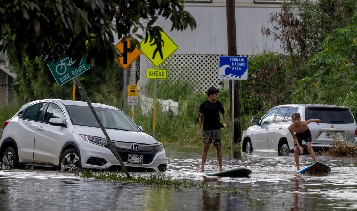 Zwei Jugendliche surfen in Waialua neben einem liegengebliebenen Fahrzeug im Hochwasser.