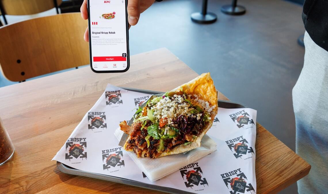 Zwei Mal Krispy Kebab: einmal auf dem Smartphone in der KFC-App und einmal auf einem Tablett in einer Krispy-Kebab-Filiale.